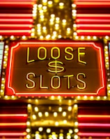 Bright neon lights display the words 'Loose Slots' with a dollar sign in the center. The sign is outlined with bulbs, creating a vibrant and flashy effect typical of a casino or entertainment venue.