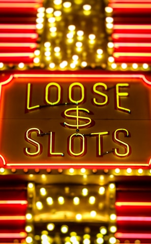 Bright neon lights display the words 'Loose Slots' with a dollar sign in the center. The sign is outlined with bulbs, creating a vibrant and flashy effect typical of a casino or entertainment venue.