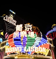 Bright neon signs in multiple colors illuminate the night, prominently displaying the name 'Casino Lisboa' alongside signage in Chinese characters. The lights form intricate patterns and vibrant displays, creating a lively and energetic atmosphere.